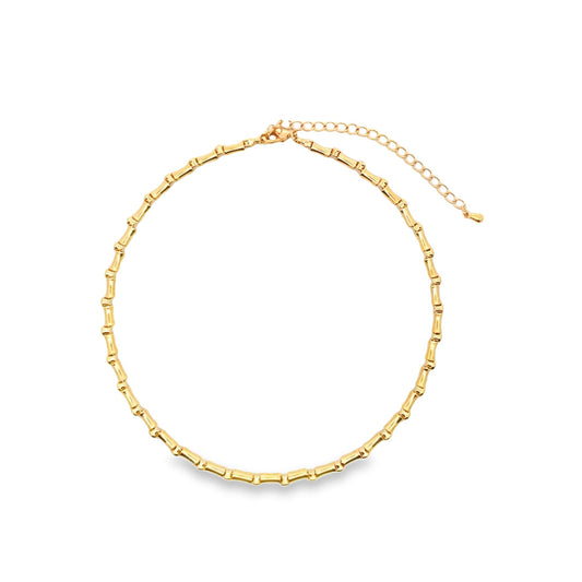A polished gold bamboo choker necklace rests on a plain white background, highlighting its textured, segmented design.