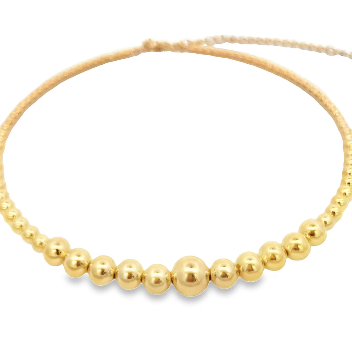 A delicate gold bead bracelet features a string of polished spherical beads graduating in size toward the center, displayed against a clean white background.