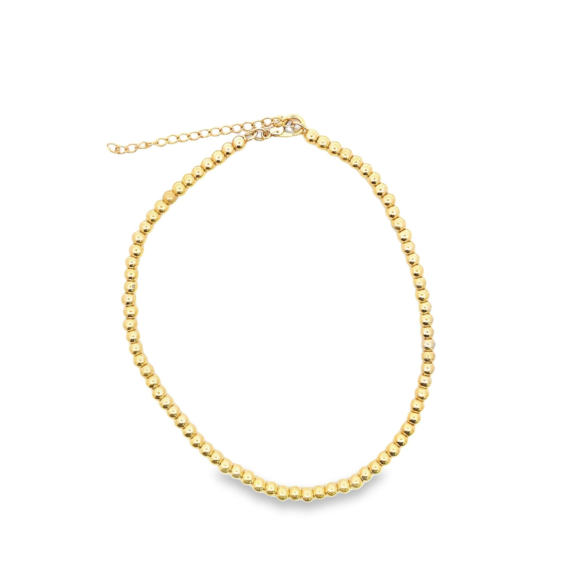 A delicate gold beaded necklace rests in a circle against a clean white background, showcasing its shiny metallic spheres and adjustable chain.