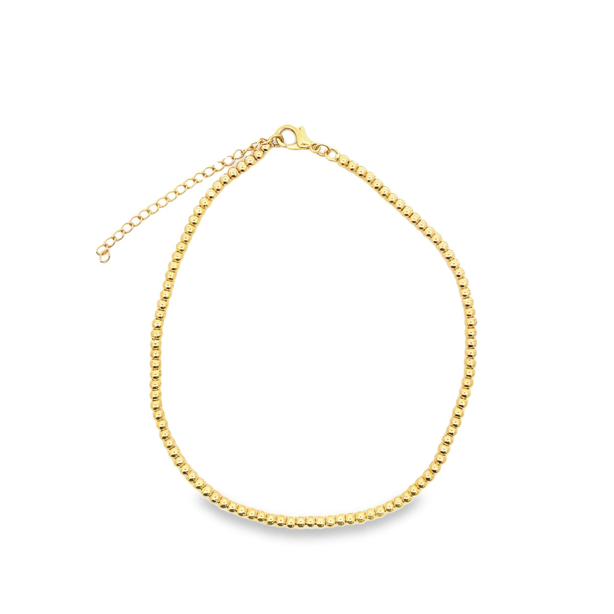 A delicate gold bead choker necklace rests in a circular display against a clean white background, showcasing its glossy metallic spheres and adjustable chain clasp.