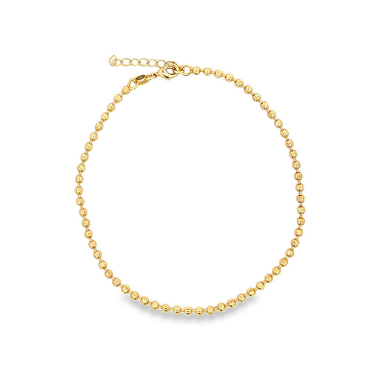 A gold bead chain anklet rests in a complete circle on a clean white background.