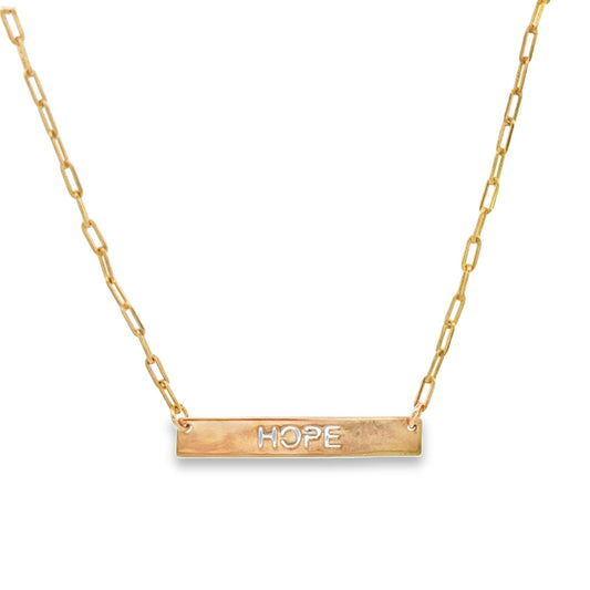 A delicate gold paperclip chain necklace features a horizontal bar pendant engraved with the word HOPE.