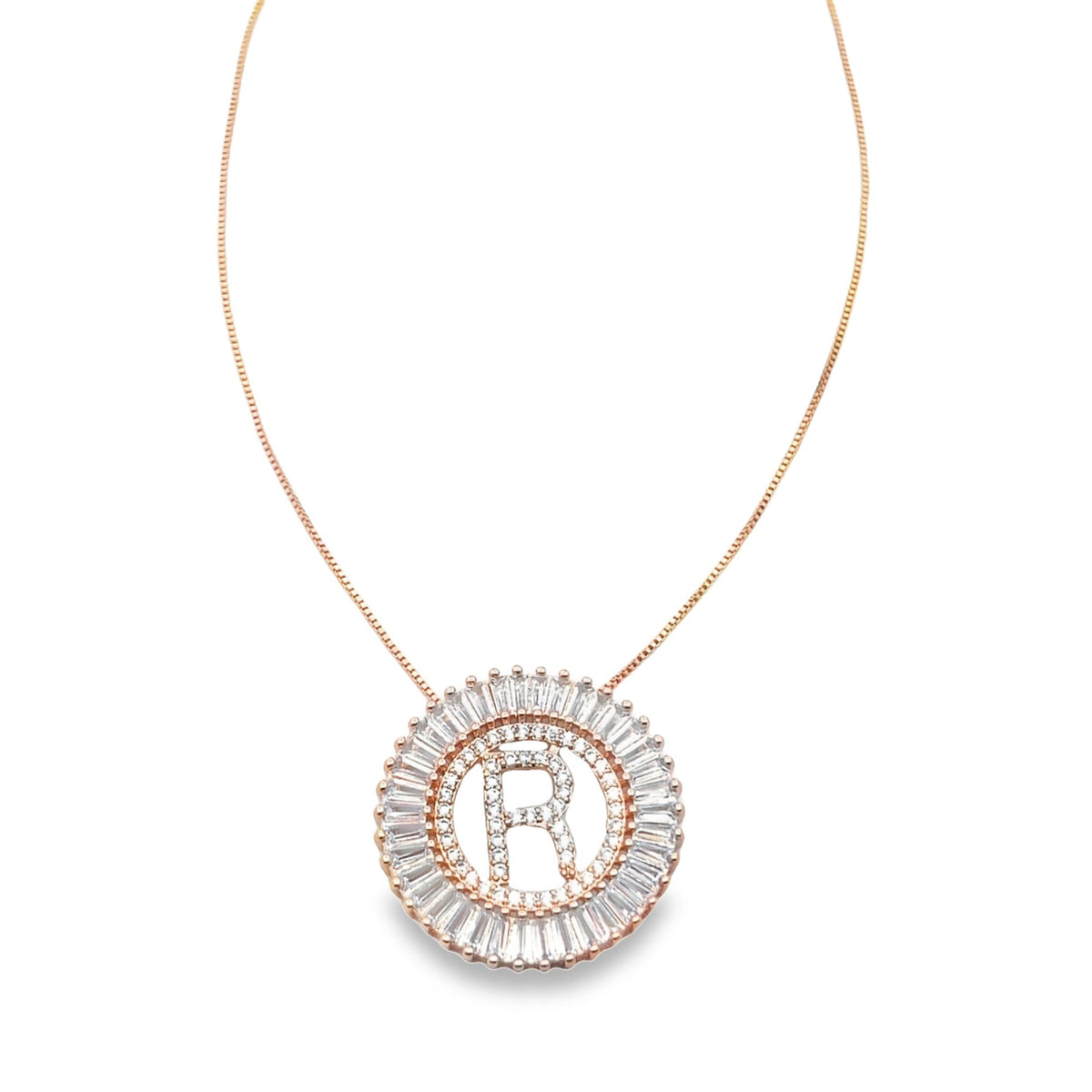 A delicate rose gold chain holds a circular diamond pendant featuring the initial R.