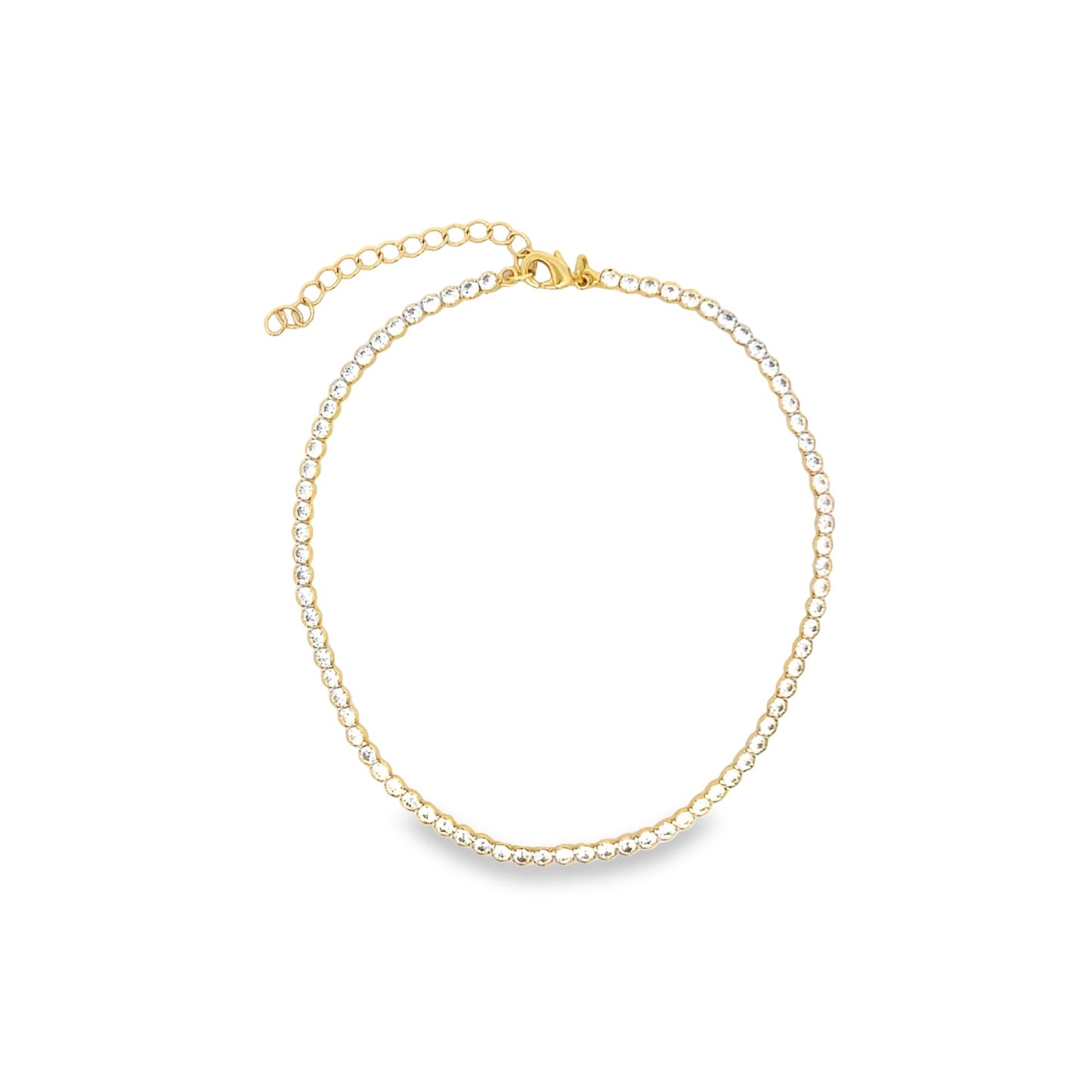 A gold tennis necklace featuring a continuous line of sparkling clear rhinestones rests in a circle on a white background.
