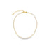 A gold tennis necklace featuring a continuous line of sparkling clear rhinestones rests in a circle on a white background.
