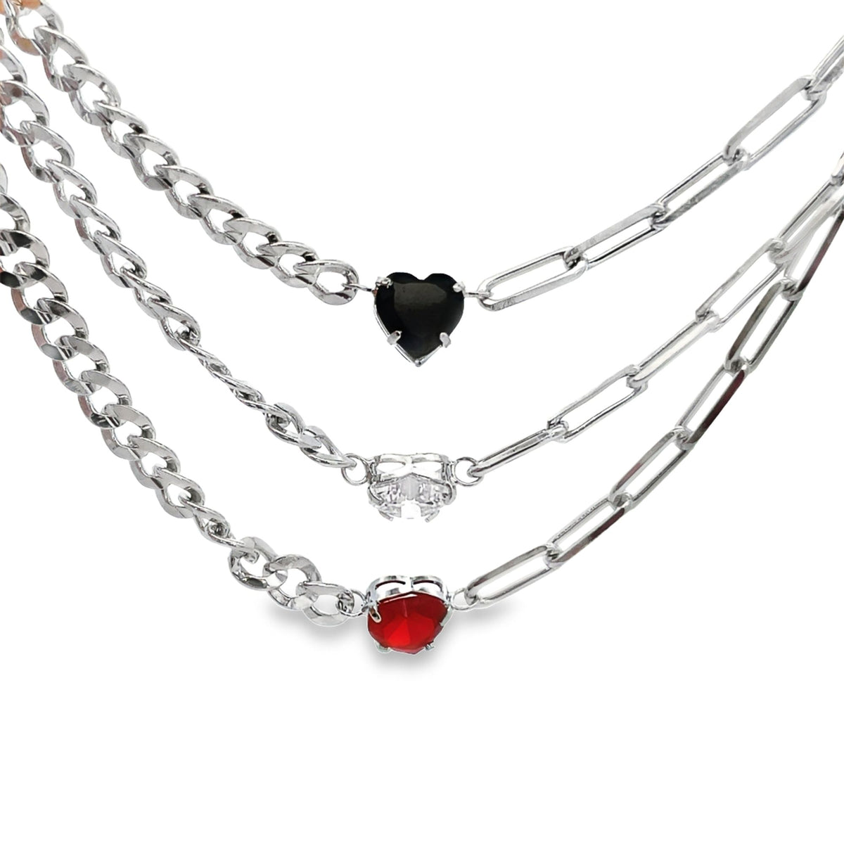 A layered silver chain necklace features three distinct heart-shaped pendants in black, clear, and red.