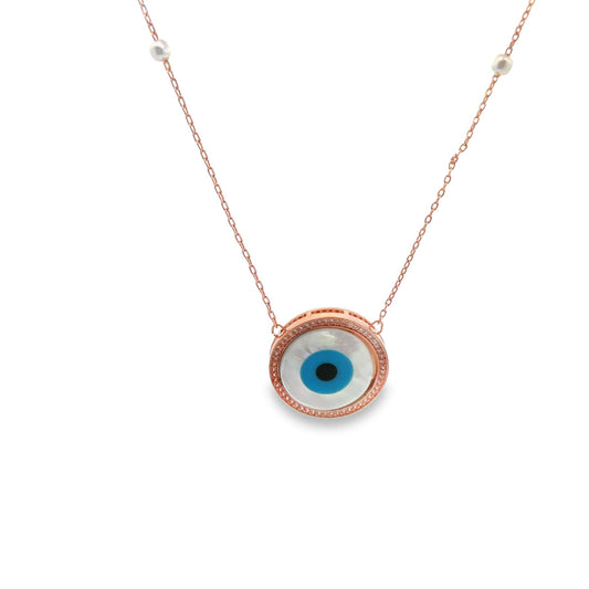 A delicate rose gold evil eye necklace hangs against a white background, featuring a round blue and white glass pendant adorned with tiny crystals and small pearls on the chain.