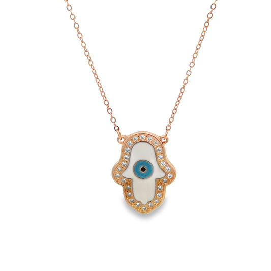A delicate rose gold Hamsa hand necklace features a white enamel center, sparkling diamond accents, and a protective blue evil eye charm.