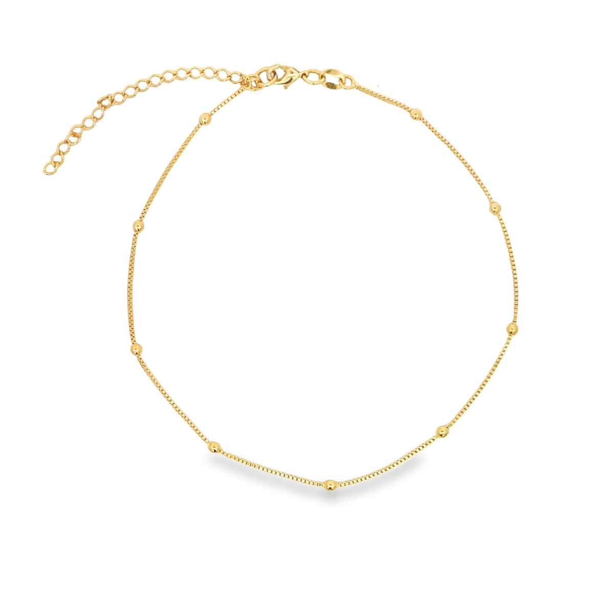 A delicate gold chain anklet adorned with evenly spaced small beads lies displayed against a clean white background.