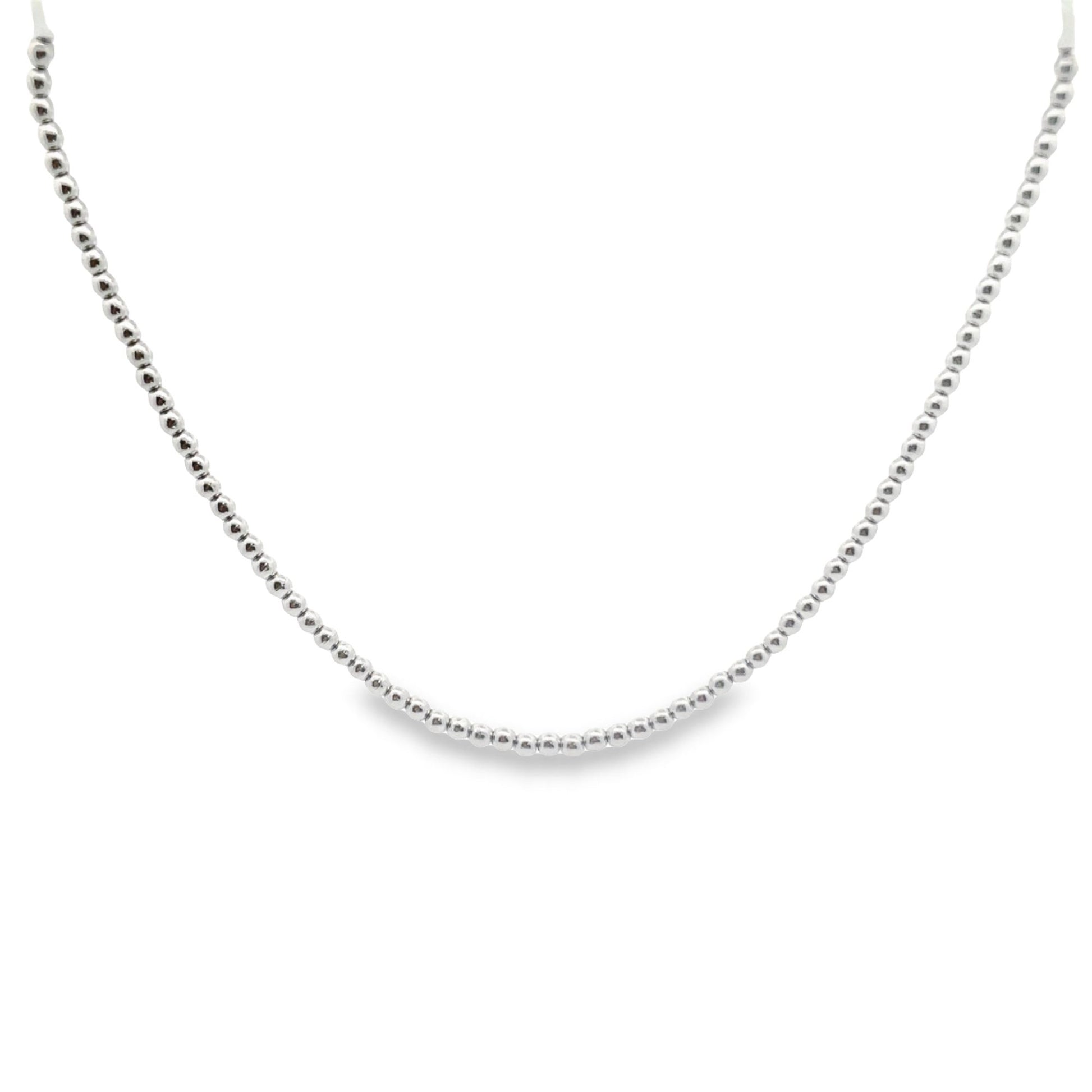 A delicate silver beaded chain necklace curves gracefully against a clean white background.