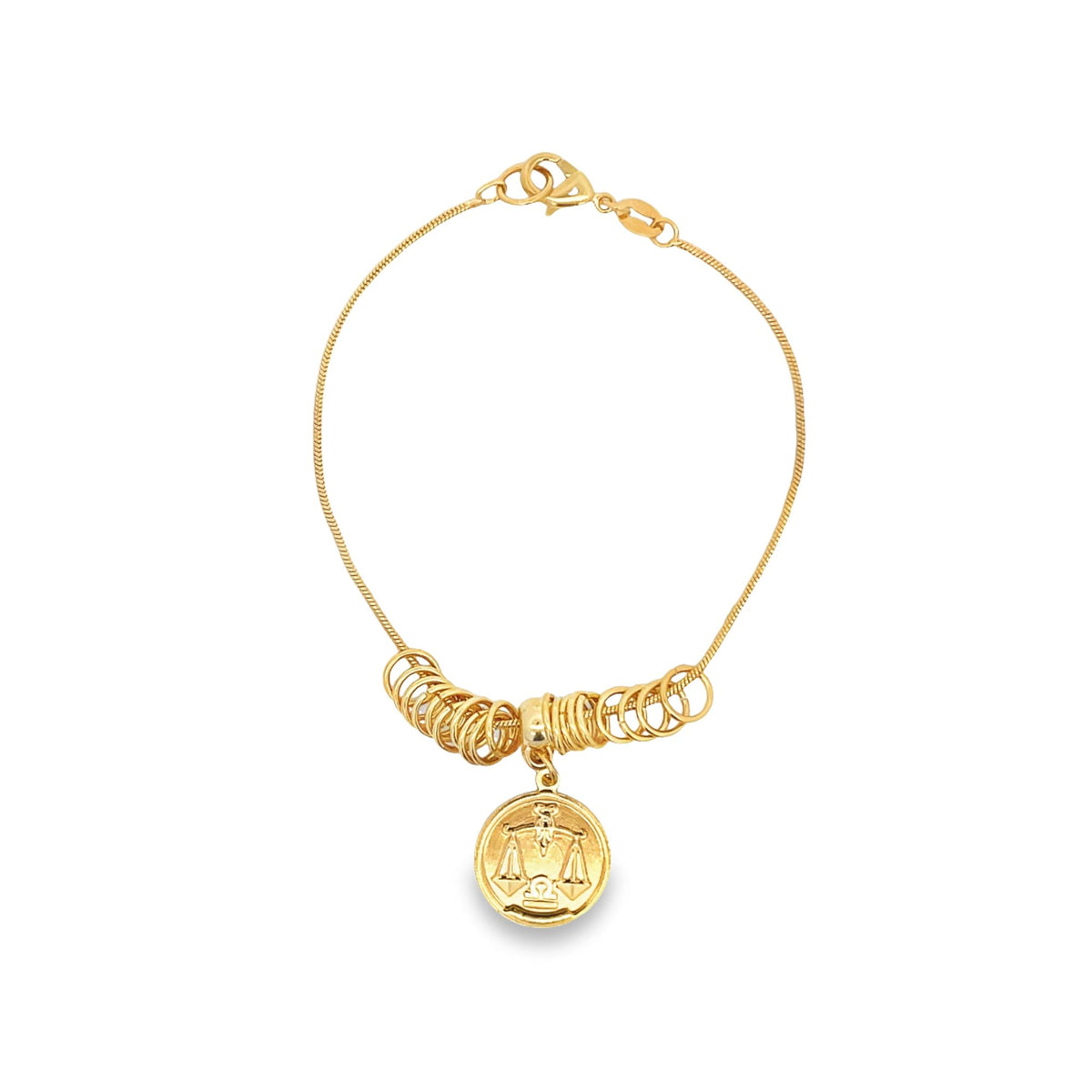 A delicate gold charm bracelet displays a round Libra zodiac pendant suspended among a cluster of small golden rings.