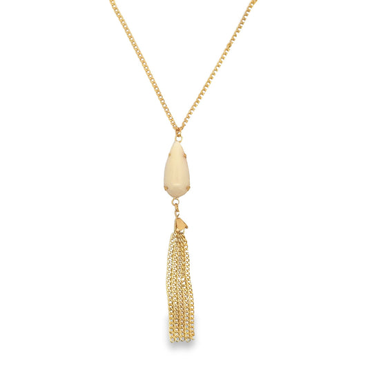 A gold chain necklace features a pear-shaped cream stone pendant with a delicate tassel dangling below.