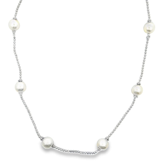 A delicate silver chain necklace features evenly spaced, luminous white pearls against a plain white background.