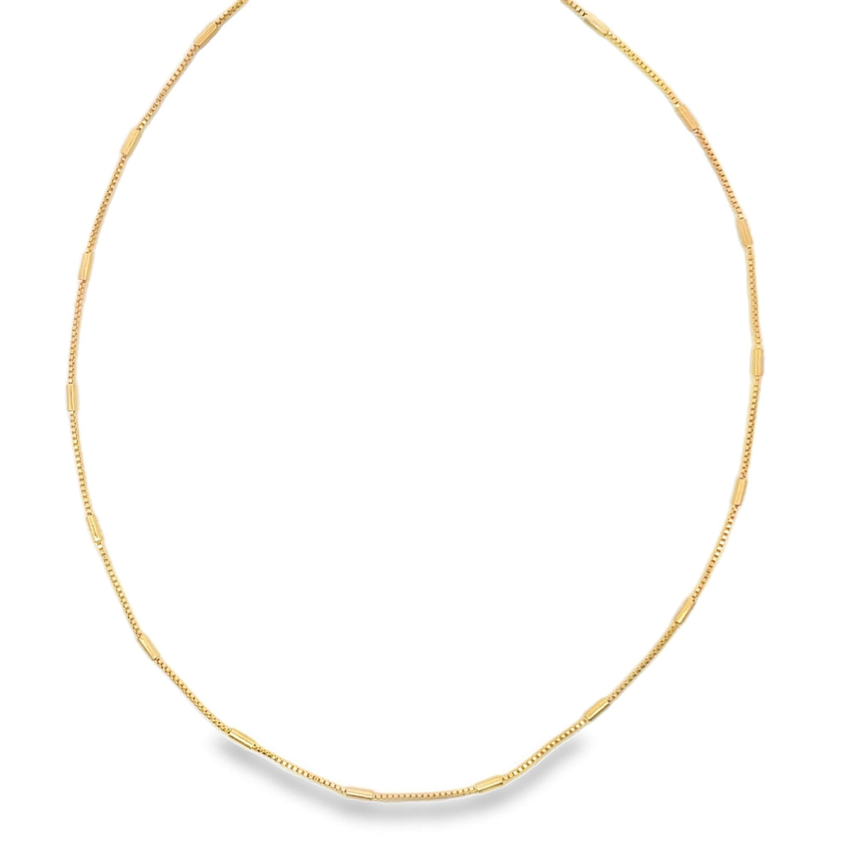 A delicate gold chain necklace with evenly spaced cylindrical bar accents rests in a circular shape against a white background.