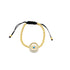 A delicate gold bead bracelet features a sparkling evil eye charm and adjustable black cord ties against a clean white background.