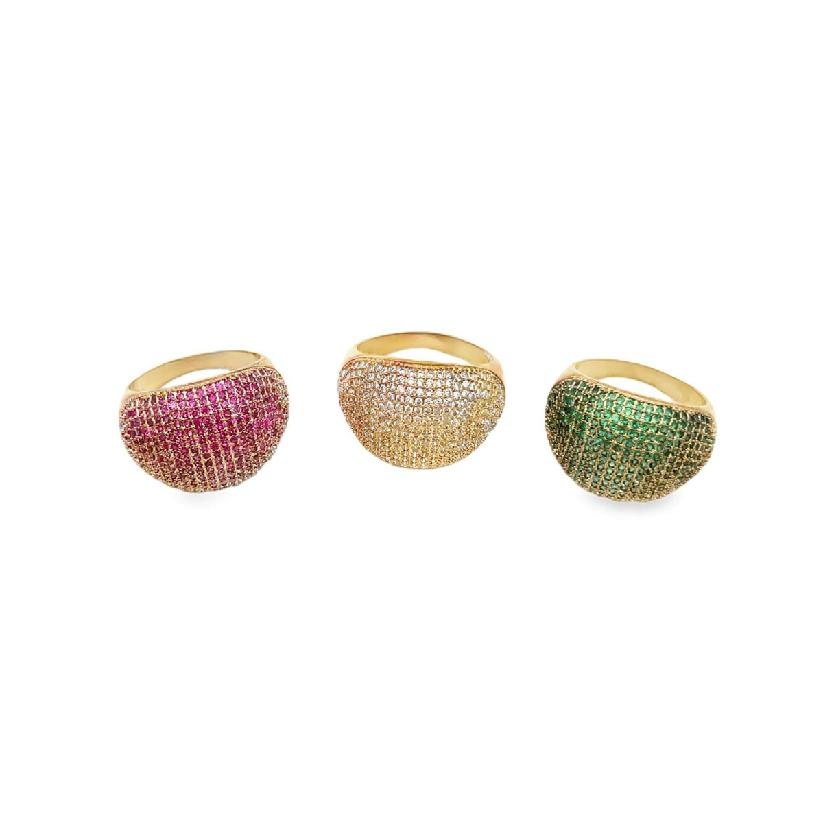 Three gold dome cocktail rings sparkle against a white background, featuring pavé-set pink rubies, white diamonds, and green emeralds.