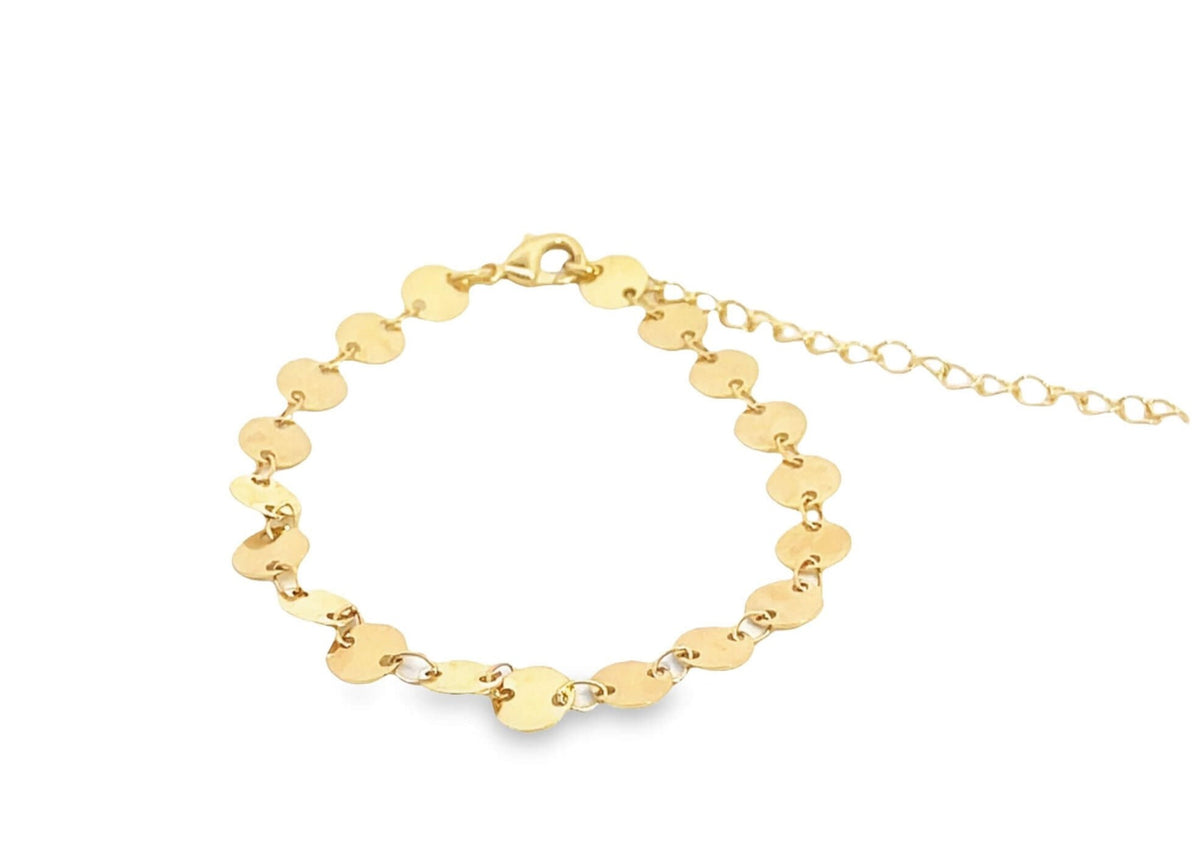 A delicate gold disc bracelet rests on a white background, featuring a chain of small, shimmering coin charms.