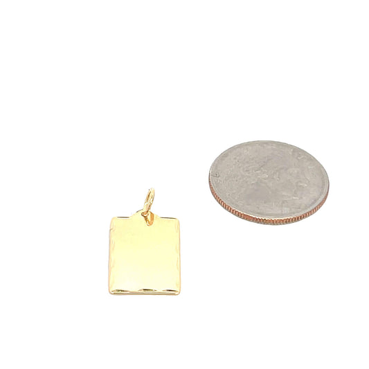 A small gold rectangular tag pendant rests next to a US quarter coin for size comparison on a white background.