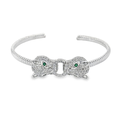 A silver pave diamond panther cuff bracelet features two facing leopard heads embellished with green emerald eyes against a clean white background.