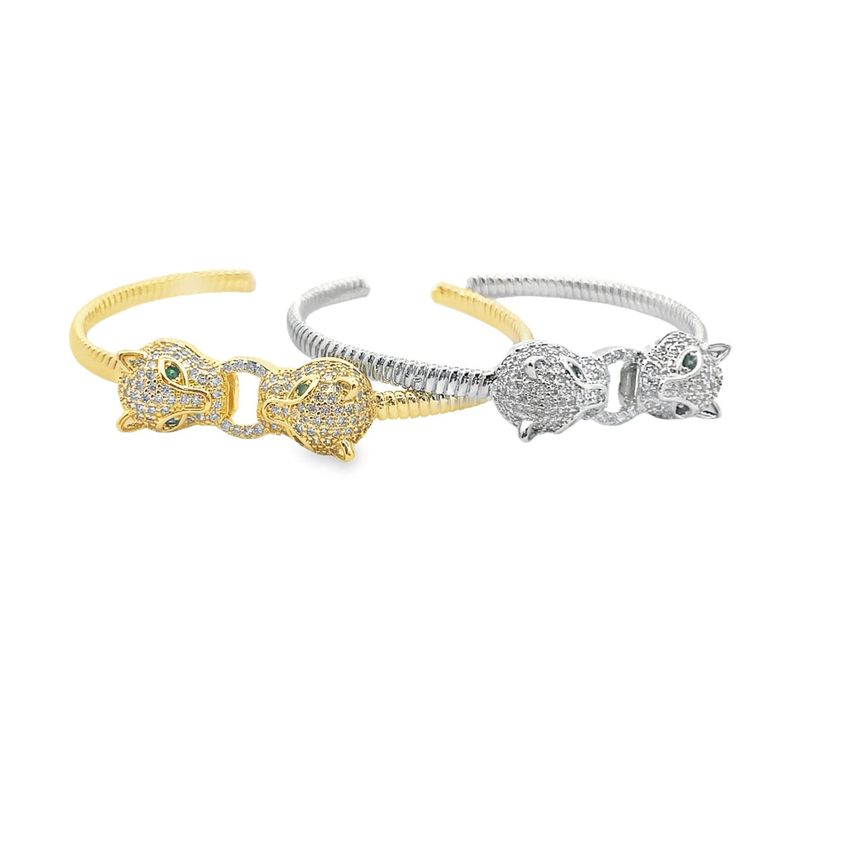 Two interlocking panther cuff bracelets featuring diamond pavé and emerald eyes rest on a white background, one in gleaming gold and the other in sleek silver.