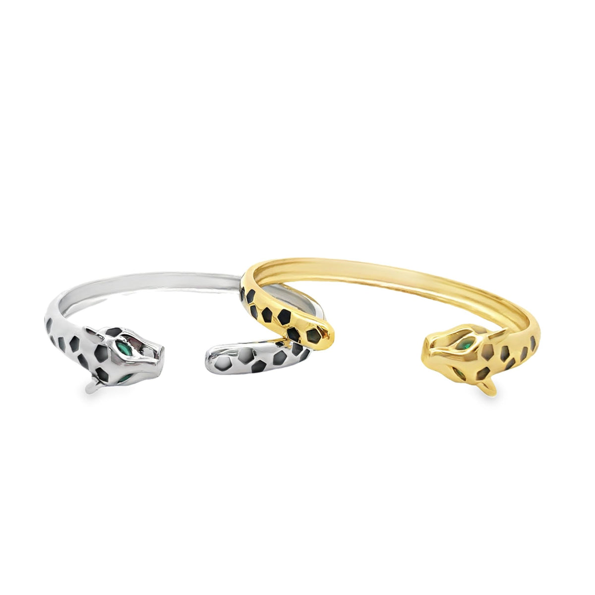 Two panther-shaped open bangles, one in silver and one in gold with black spots and green gemstone eyes, rest side by side against a white background.