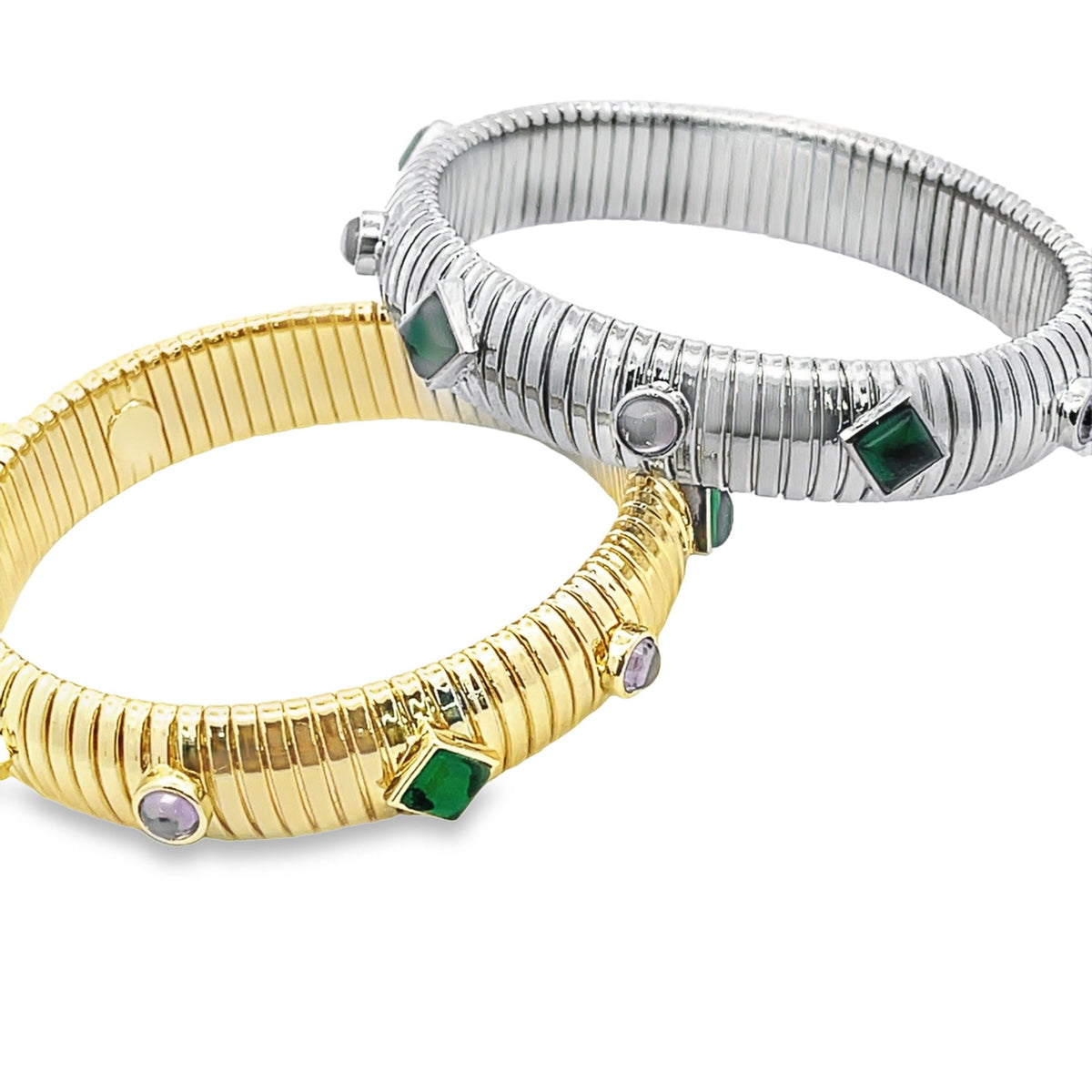 Two ribbed expansion bracelets, one in gold and one in silver, sparkle with embedded green and purple gemstones against a clean white background.
