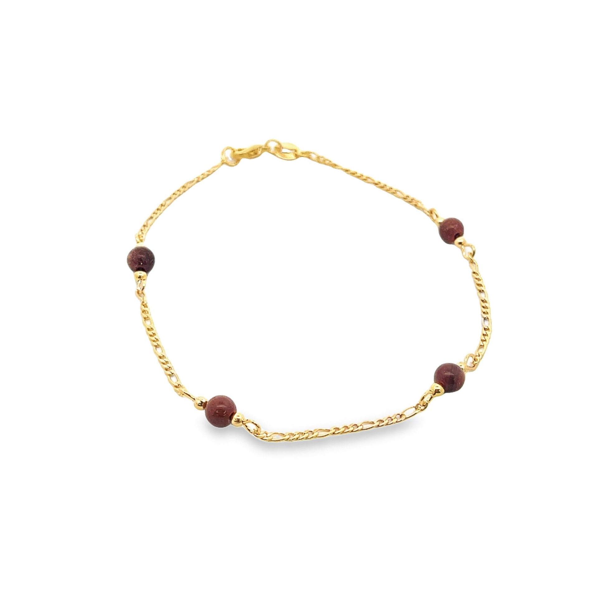 A delicate gold link bracelet features small, deep red gemstone beads evenly spaced along the chain against a white background.