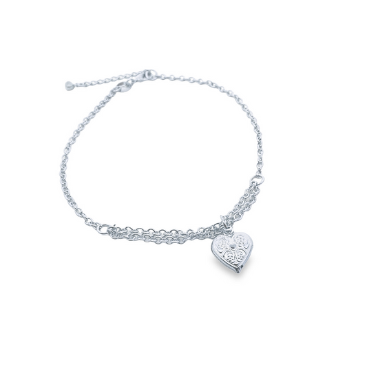 A delicate silver anklet features a layered chain design and a detailed heart locket charm against a white background.