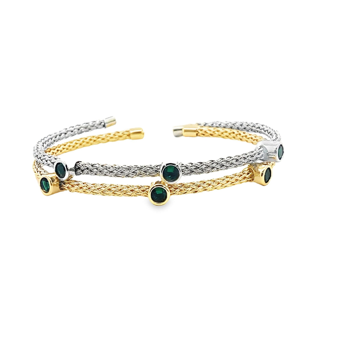 Two interwoven gold and silver braided cuff bracelets showcase sparkling emerald green gemstones bezel-set along their bands against a clean white background.
