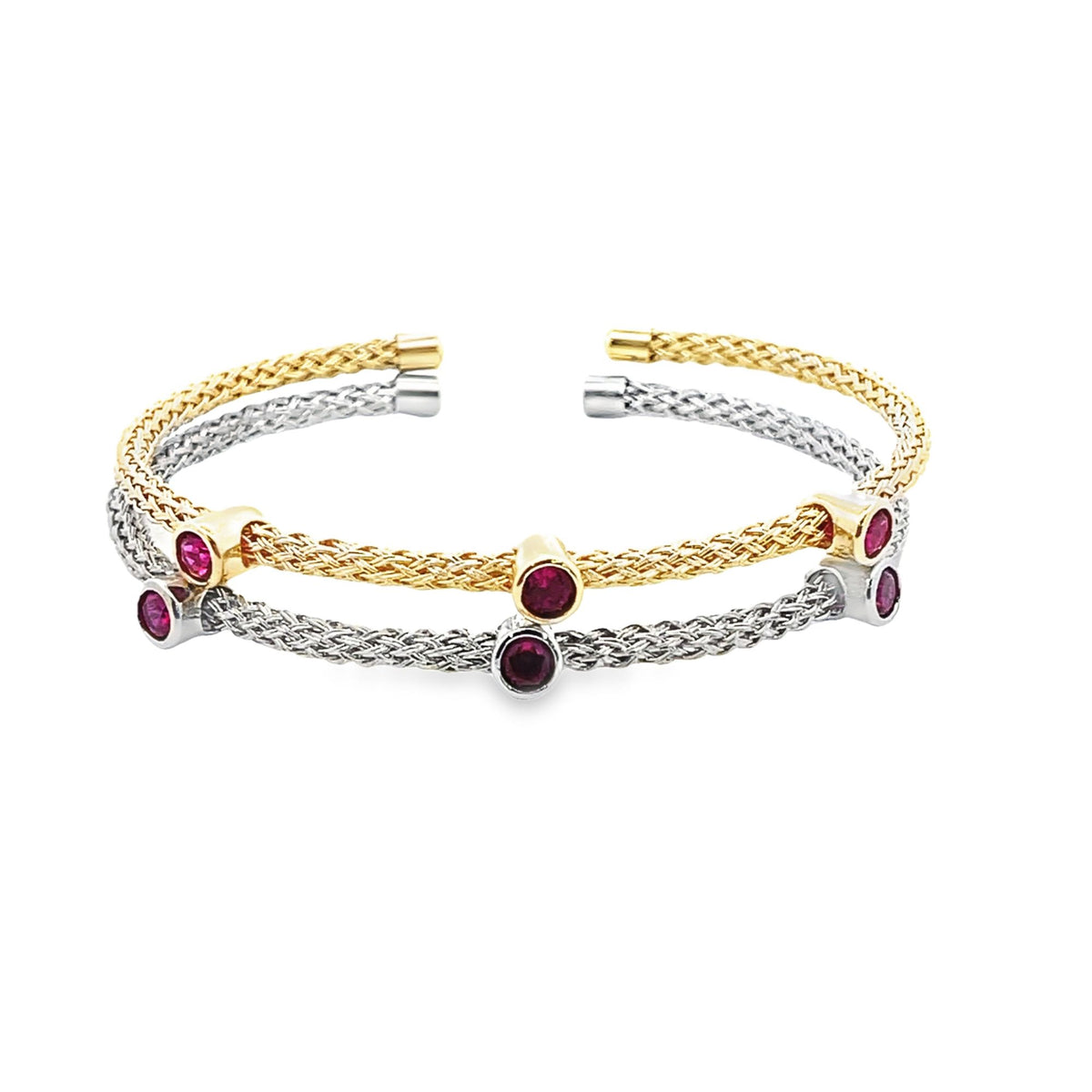 Two intertwined woven metal cuff bracelets, one in yellow gold and one in white gold, feature bezel-set round ruby gemstones against a plain white background.