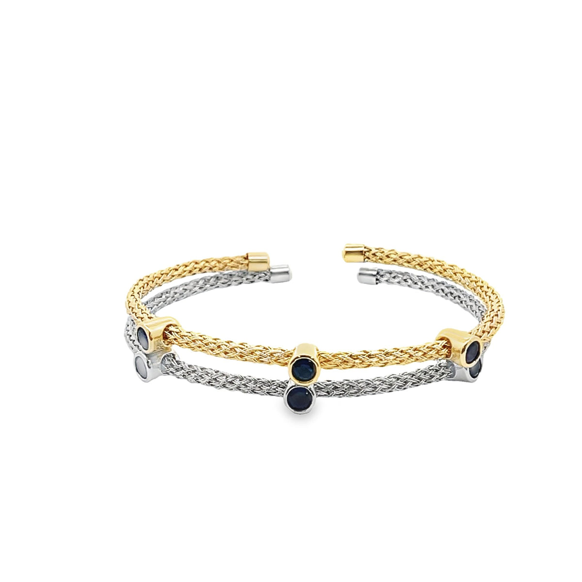 A double-strand woven cuff bracelet crafted in yellow gold and sterling silver features dark blue sapphire gemstones evenly spaced along the bands.