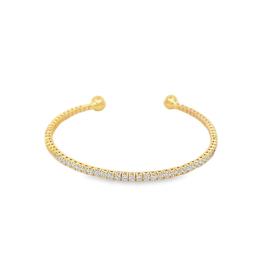 A gold cuff bracelet sparkles with a continuous line of tiny diamonds and features polished ball ends against a white background.