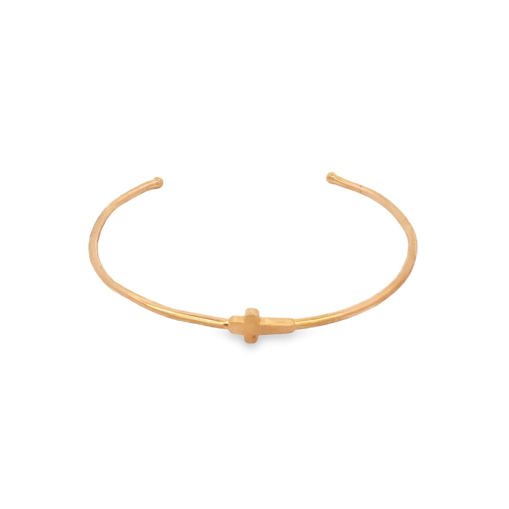 A delicate gold cuff bracelet features a small cross charm centered on the band against a clean white background.