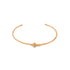 A delicate gold cuff bracelet features a small cross charm centered on the band against a clean white background.