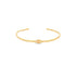 A minimalist gold cuff bracelet features a delicate evil eye motif centered on the band against a clean white background.