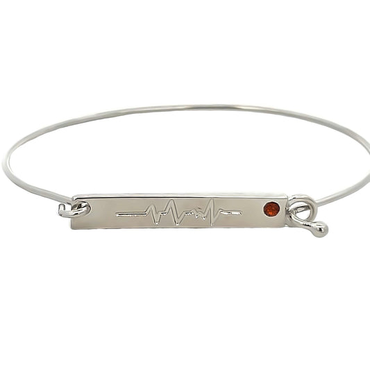 A sleek silver bangle bracelet features an engraved heartbeat EKG line and a sparkling red gemstone accent on a rectangular bar charm.