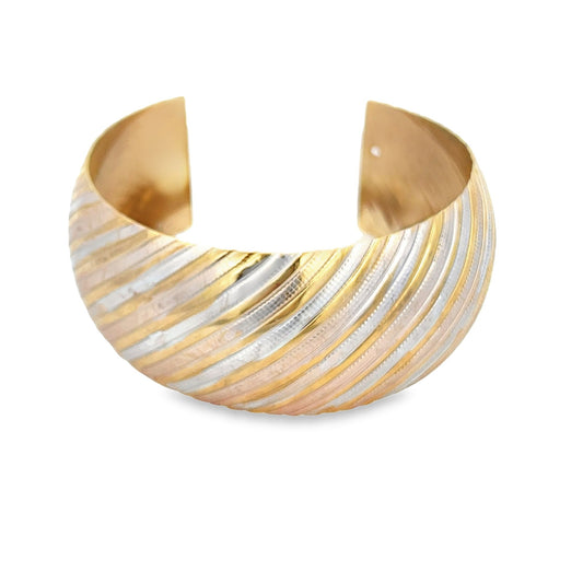 A wide tri-color gold cuff bracelet features diagonal stripes of yellow, white, and rose gold in a textured design.