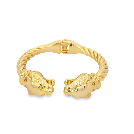 A polished gold-tone metal cuff bracelet features twisted cable details and matching opposing jaguar animal head terminals against a clean white background.