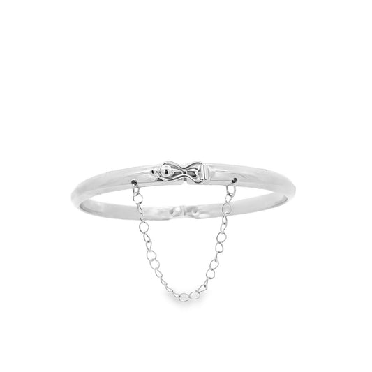 A polished silver bangle bracelet features a secure clasp and a delicate dangling safety chain against a clean white background.