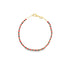 A delicate gold beaded bracelet features alternating red and black seed beads arranged in a vibrant pattern against a white background.