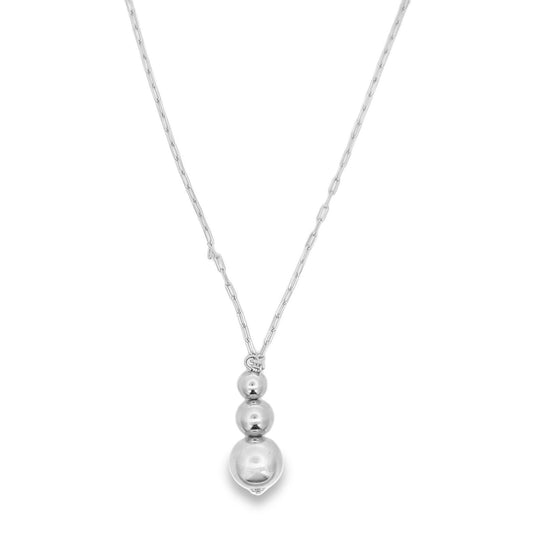 A delicate silver chain necklace features a vertical drop pendant made of three graduated polished metal spheres.