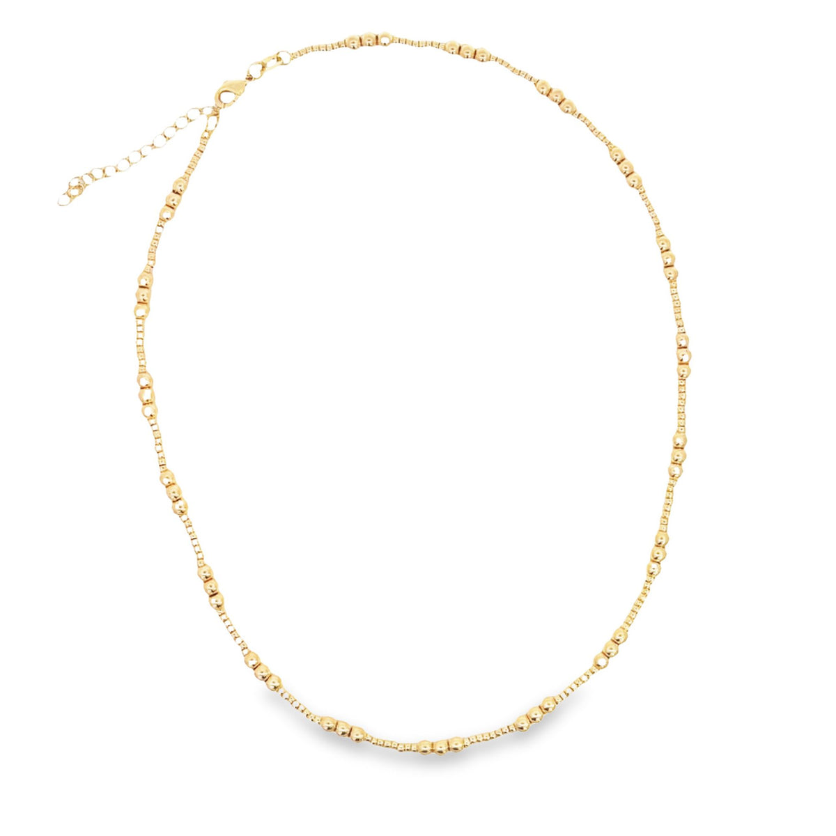 A delicate gold beaded necklace rests in a circle against a white background, showcasing its intricate texture and clasp.