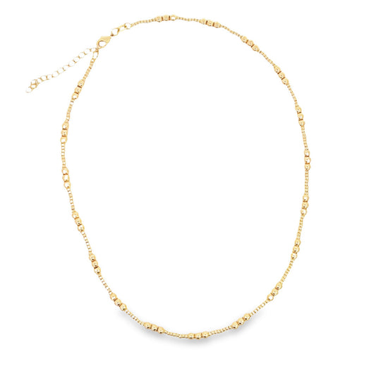 A delicate gold beaded necklace rests in a circle against a white background, showcasing its intricate texture and clasp.