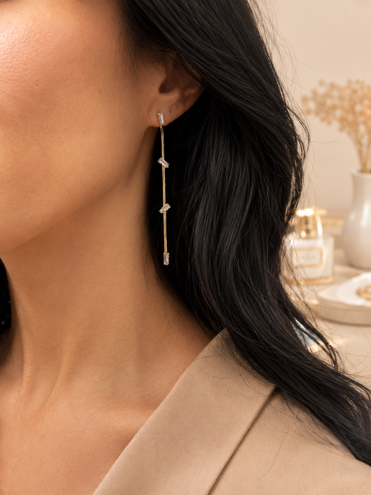 A woman with dark hair wears a delicate gold dangle earring adorned with sparkling baguette-cut stones.