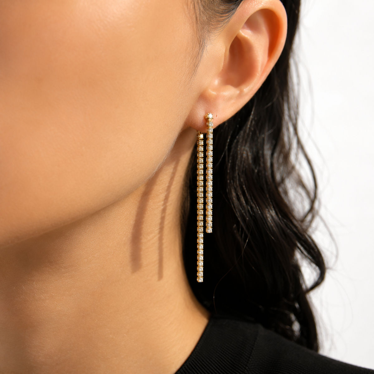 A woman wears sparkling gold and diamond tennis chain drop earrings.