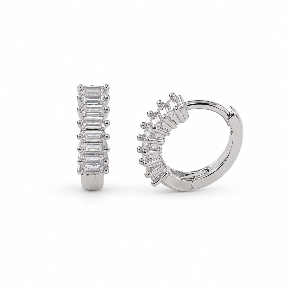 A pair of silver huggie hoop earrings featuring sparkling baguette-cut zirconia stones gleams against a white background.