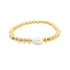 A gold beaded stretch bracelet features a central teardrop-shaped baroque pearl.