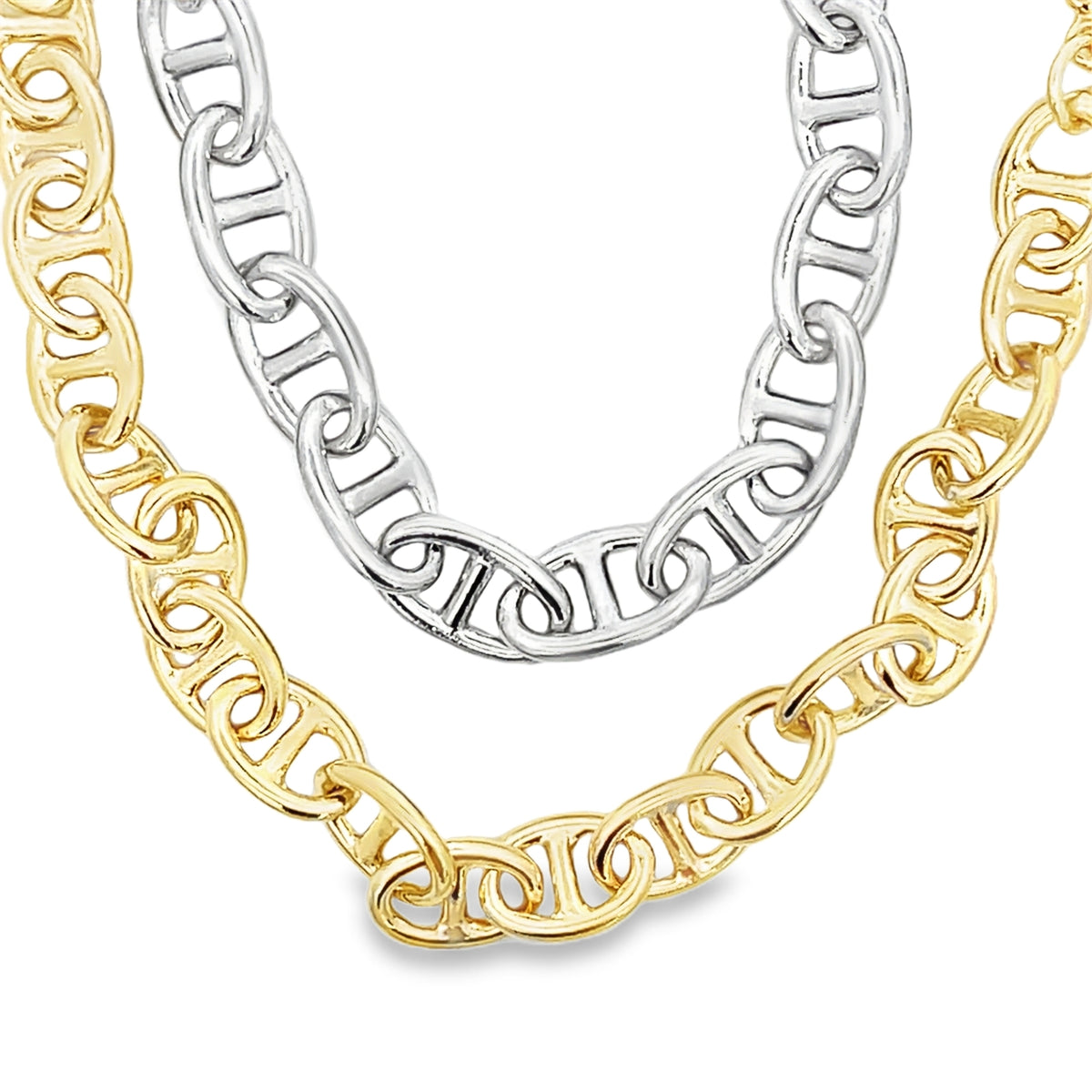 Two chunky mariner chain necklaces, one in silver and one in gold, drape gracefully against a plain white background.