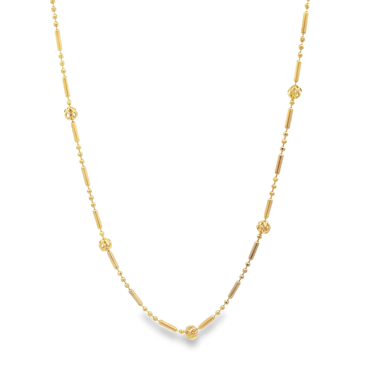 A delicate gold necklace features alternating small beads, cylindrical bars, and textured spheres against a white background.