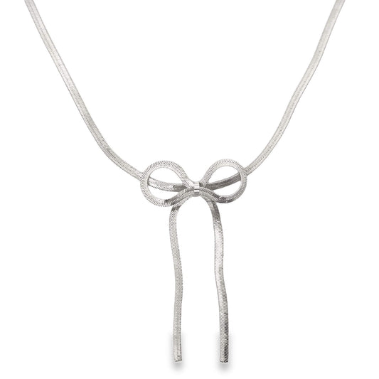 A delicate silver herringbone chain necklace features a stylish bow pendant hanging against a plain white background.